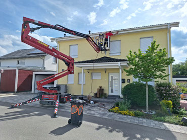 Gelenk-Teleskopbühne vor einem Wohnhaus mit einem Arbeiter, der die Dachrinne reinigt