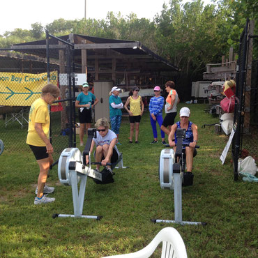 two guests practice on the erg as a club member watches