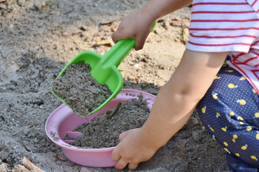 Kind spielt im Sandkasten, nur der untere Körper sichtbar