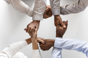 Vier Mitarbeiter überkreuzen ihre Arme und geben sich dabei die Hände als Zeichen für mehr Business Skills 