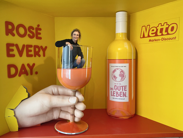 Kulisse für Nettomarkt mit Weinflasche, Hand, Weinglas zum Drinsitzen