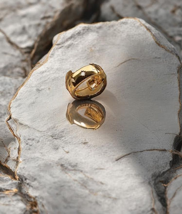 MOKOŠEV Luxusschmuck, goldener Ring mit feinen eingravierten Symbolen auf heller Steinoberfläche mit Spiegelung.