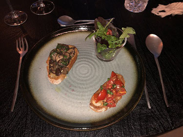 Foto von der Vorspeise auf dem Teller, zweierlei Bruschetta mit Rucola-Salat. 