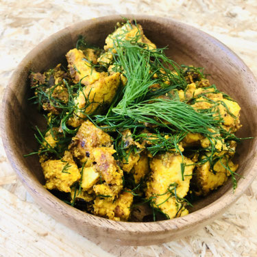 Rührtofu. Durch Kurkuma gelb eingefärbtes Tofu in einer braunen Holzschale. Oben auf liegt frischer grüner Dill und rundet das Gesamtbild ab.