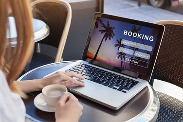 Frau sitzt am Laptop und bucht eine Ferienwohnung über Booking.com und will sie mit einer Reiserücktritts-Versicherung der ERGO absichern