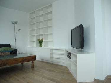 Schrankwand mit offen gestalteten Fächern und Schubladen und integriertem TV-Sideboard. Möbel eingepasst in vorhandene Raumsituation mit winkeliger Wandführung.