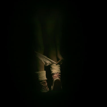 Dettaglio di corpo femminile che emerge dall'oscurità, fotografia intima in stile chiaroscuro di Alessandro Tintori.