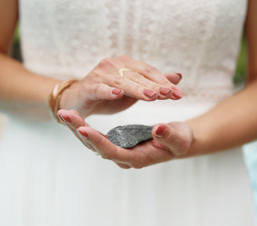 Cérémonie laïque des pierres. La mariée magnétise sa pierre. Elle tient une pierre dans sa main gauche et la magnétise de sa main droite. Elle porte un vernis à ongles vieux rose.