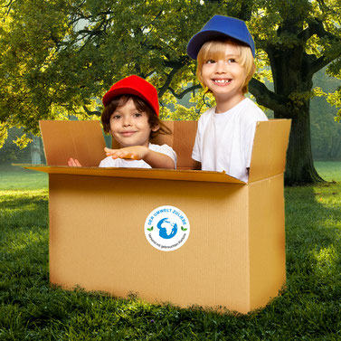 meinAufkleberladen - Verpackungsaufkleber blaue Erde - Der Umwelt zuliebe - Versand mit gebrauchten Kartons - klebt auf gebrauchten Karton in dem 2 Kinder spielen, Karton steht auf grüner Wiese mit großem Baum
