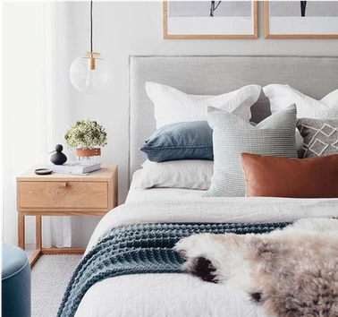 Doppelbett mit neutraler Bettwäsche und einem blauen, strukturiertem Überwurf