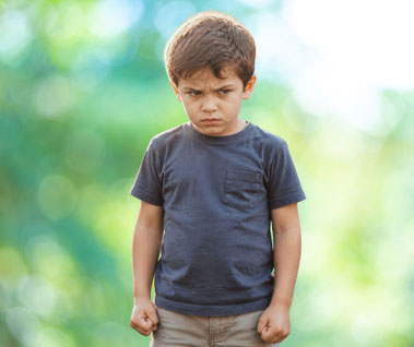 Ein kleines Kind mit Wut und trotzigem Gesichtsausdruck steht draußen alleine, mit herunterhängenden Armen, die Hände zu Fäusten geballt, als Symbol für Suche nach Schutz, Anerkennung, Liebe und verständnisvoller Begleitung von Emotionen - mein schützling
