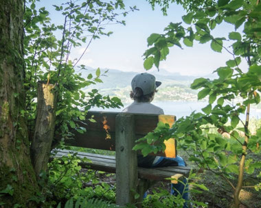 Familienurlaub am Mondsee-Irrsee – Kind auf Bank mit Blick auf See und Berge im Salzkammergut