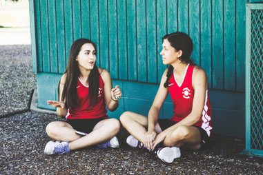 Two young women speaking to each other. They seem to be teammates, and are hopefully practicing mindful listening together.