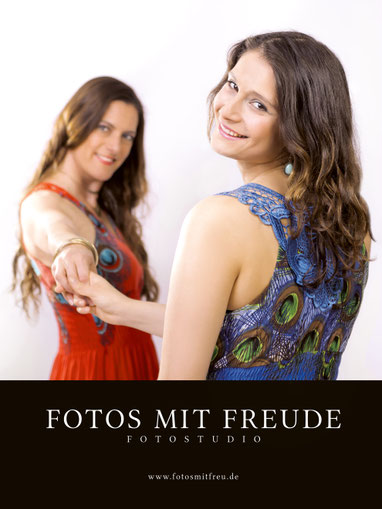 FOTOS MIT FREUDE - Eingangsschild: Zwei hübsche Frauen mit langen Haaren und schönen Kleidern halten sich die Hand und lächeln freundlich in die Kamera und empfangen so die Kundin