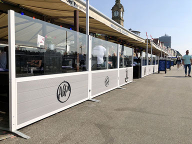 Windschutz-System für die Gastronomie mit grauen Paneelen und Logo-Druck an einer Promenade