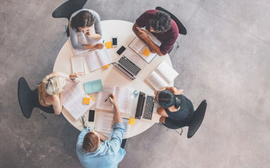 Mehrere Hände arbeiten gemeinsam an Strategien und Layouts auf einem Tisch – visuell als Symbol für Veränderungsprozesse in KMUs und Teams im Wandel.