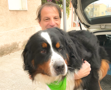 Sportmentaltrainer steht vor dem Wagen und hält Berner Sennenhund im Arm