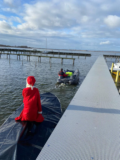 Eine noch hinten zu sehende Nikolaus-Figur wird auf einem Boot von einem Motorboot auf einem See gezogen.