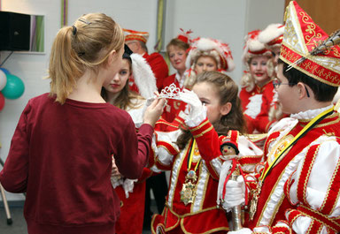 Prinzessin Merit I (Merit Römer) überreicht ihrer Nachfolgerin Prinzessin Xenia I (Xenia Zimmermann) die Insignien der Macht, Diadem und Blumenstrauß. Prinz Benedikt II (re.) trägt bereits die Narrenkappe auf dem Kopf und hält das Zepter fest in Händen.