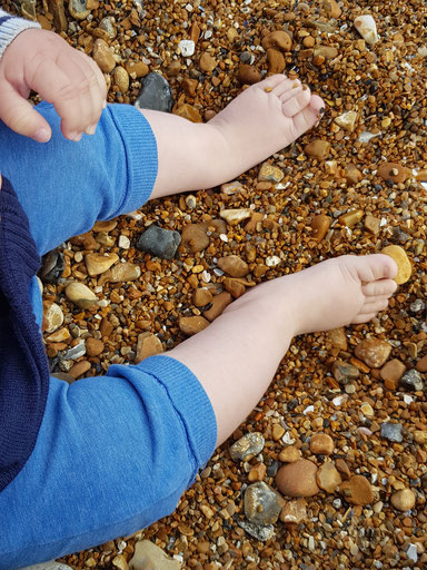 Ein Baby sitzt am Strand mit nackigen Füßen.