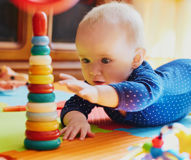 Ein Baby, das auf dem Bauch liegend mit schönen Spielmaterialien aus Holz spielt, symbolisch für Pikler, Montessori und Pikler bei mein schützling, München