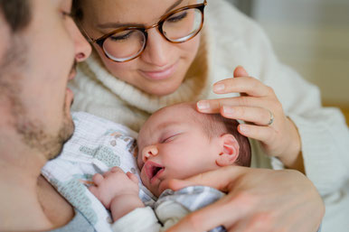 Junge Eltern schauen liebevoll auf ihr schlafendes Neugeborenes und genießen den ruhigen Moment