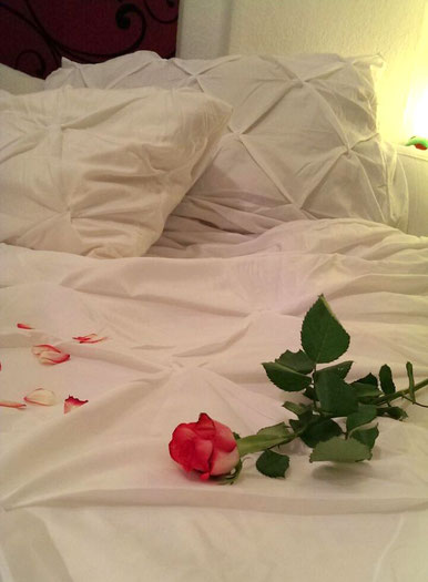 Ein weißes Bett mit roter Rose und verstreuten Blütenblättern, ein Sinnbild für Romantik