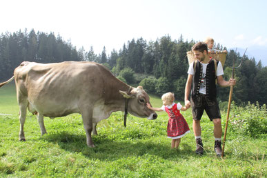 Ein Mann und ein kleines Mädchen auf einer Almwiese, das Mädchen streichelt eine Kuh.