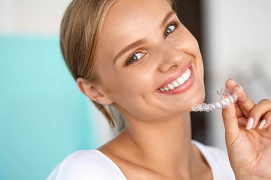 Lachende Frau zeigt ihre transparente Invisalign Zahnschiene beim Kieferorthopäden Gröbenzell, Dr. Richard Wiesner.