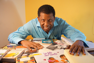 Das Bild zeigt den Autor Dany Laferrière hinter einem Tisch voller Bücher.