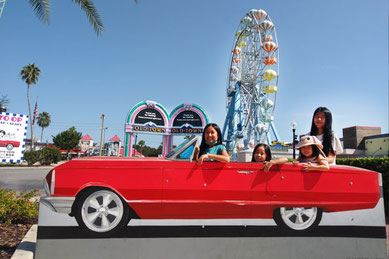 オールド・タウン キシミー（Old Town Kissimmee）の入口で撮影された写真。赤いクラシックカー型のフォトスポットに子どもたちが楽しそうに並び、背景には観覧車や「OLD TOWN」のカラフルなゲートが見える。クラシックな街並みを再現したショッピング＆エンタメスポットで、週末のクラシックカーショーやアトラクションも楽しめる人気エリア。