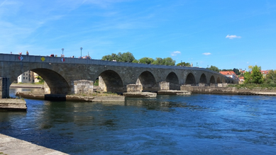 Steinerne Brücke in Regensburg mit der dunkelblauen Donau und blauem Himmel
