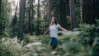 Petra Linner steht im Wald, Augen geschlossen, Arme ausgebreitet