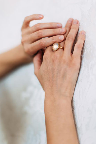 MOKOŠEV luxury jewelry, gold ring with a light crystal on a hand against a soft, light background.