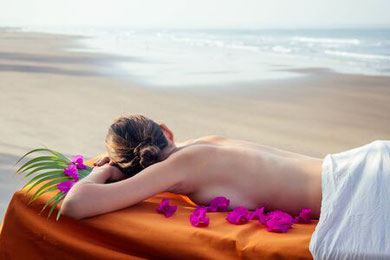 Une femme allongée sur le ventre sur un drap orange au bord de la plage, regarde la mer