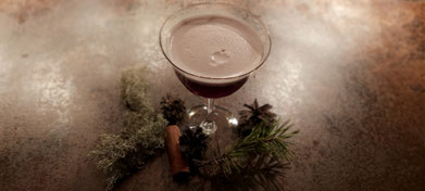 Blaubeer Cocktail Glas mit leichter Schaumkrone garniert mit Flechten auf einer dunkel glänzenden Tischplatte