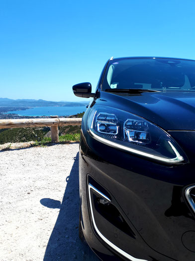 véhicule de prestige VTC Marseille exposé de face sur falaise avec vue sur mer et ciel bleu