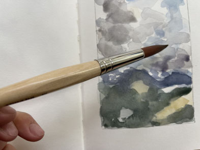 Hand, die einen Aquarellpinsel vor einem Aquarell hält