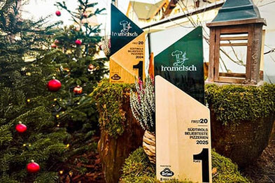 I premi della Pizzeria Trametsch a Millan: Pizzeria più amata dell'Alto Adige nel 2024 e nel 2025, presentati davanti a un albero di Natale addobbato a festa.