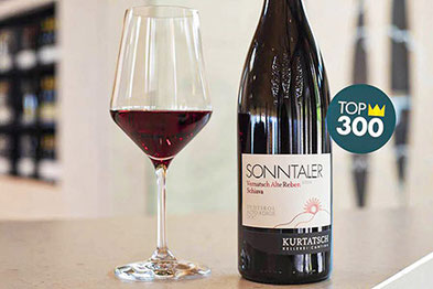 Flasche Sonntaler Vernatsch Alte Reben 2024 der Kellerei Kurtatsch neben einem gefüllten Weinglas, ausgezeichnet mit der „Corona“ von Vinibuoni d’Italia, unter den Top 300 Weinen Italiens.