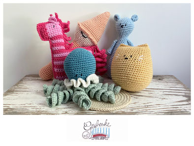 gehäkeltes Spielzeug in verschiedenen Farben präsentieren sich gemeinsam: Zebra, Oktopus, Babyrassel Krawuzi, kleiner Bär, Katze