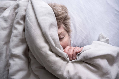 Frau liegt schlafend auf dem Rücken im Bett. Gesicht ist halb verdeckt. Porträt.