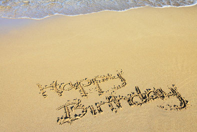 "Happy Birthday" in den Sand geschrieben, das Wasser rollt leicht im Hintergrund auf den Strand