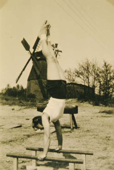 Historisches Foto mit einer Person die auf einem Turngerät turnt. Im Hintergrund sieht man eine Windmühle.