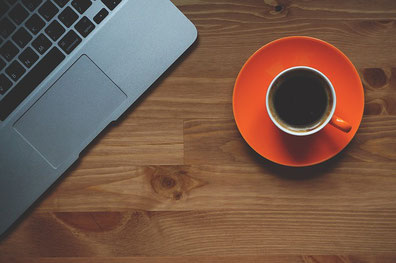 brauner Holztisch mit roter Tasse mit Untertasse und Kaffee, Laptop Tastaturausschnitt