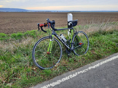 Ein Rennrad lehnt an einem Straßenpfosten. Auf dem Lenker liegen Winterhandschuhe.