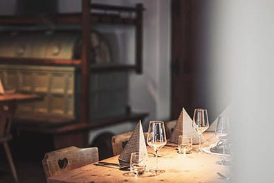 Gemütlich gedeckter Holztisch im Mesnhöf Mountain Inn mit Weingläsern, Servietten und warmem Licht, rustikale Stube mit traditionellem Südtiroler Ambiente