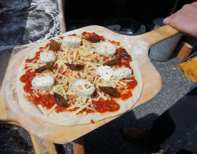 Walter de Mehlknepfle du Bar à Pizzas de Walter - traiteur évènementiel, tient une pelle à pizza en bois sur laquelle il y a une pizza au Sainte-Maure-de-Touraine.