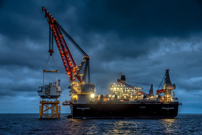 Il fait nuit et nous sommes en mer, sur le parc éolien offshore. Le Pioneering Spirit, qui est le plus gros bateau au monde d'installation offshore en mer, il dépose à l'aide d'une énorme grue, la sous-station d'EDF RENOUVELABLES sur son support.