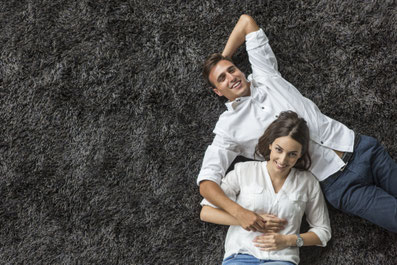 Pärchen in weißen Hemden liegt auf einem grauen flauschigem Teppichboden